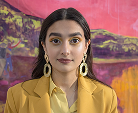 A student wearing bright colours and posing in front of a bright coloured painting